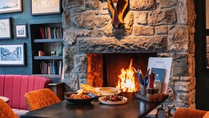 A restaurant with a stone fireplace, a menu stand, and a red cushioned bench. - The Bull and Townhouse, Beaumaris- The Inn Collection Group (Beaumaris)