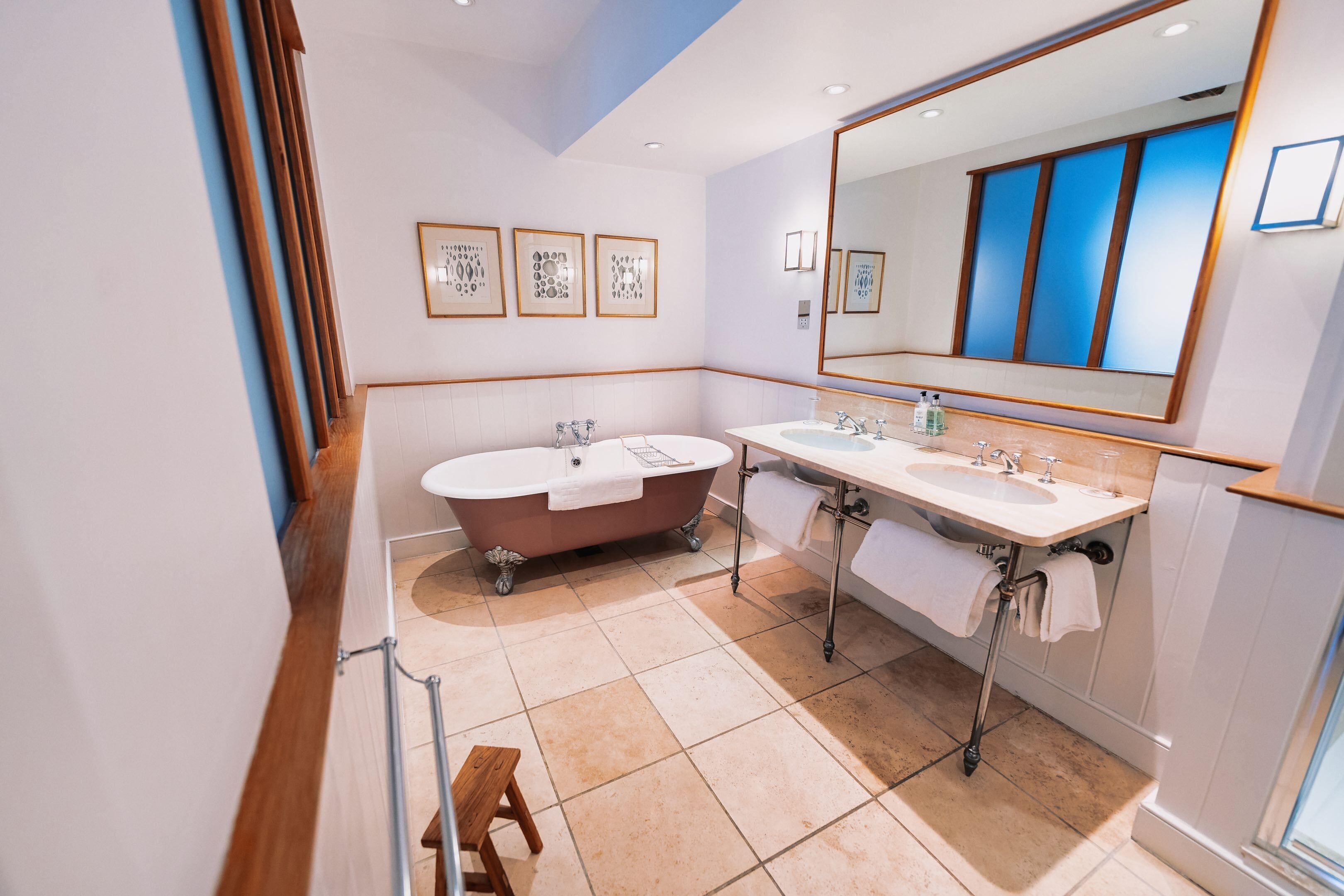 A modern bathroom with a freestanding bathtub, two sinks, and a large mirror.