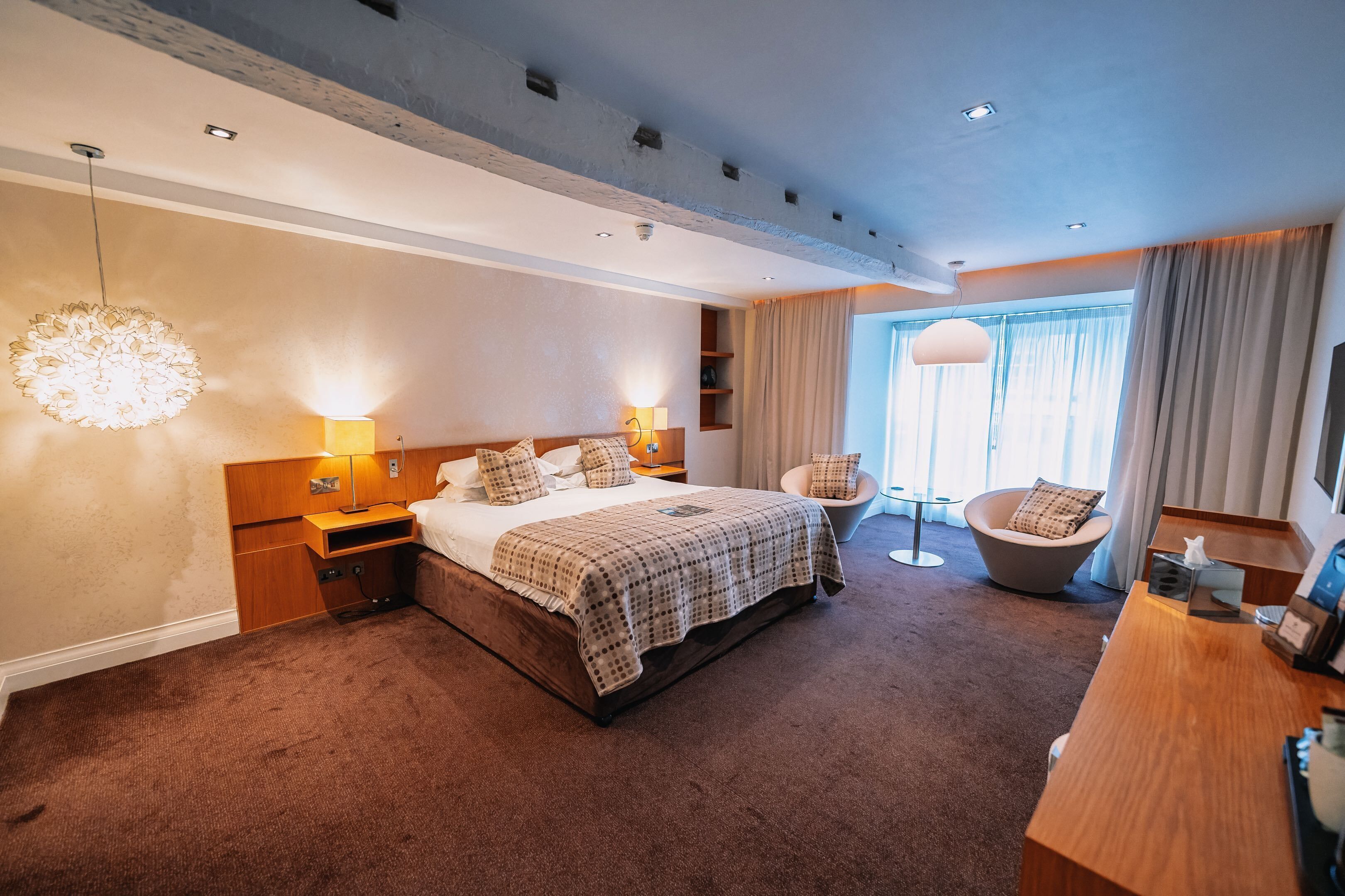 A modern hotel room with a large bed, bedside lamps, a desk, and a chair.