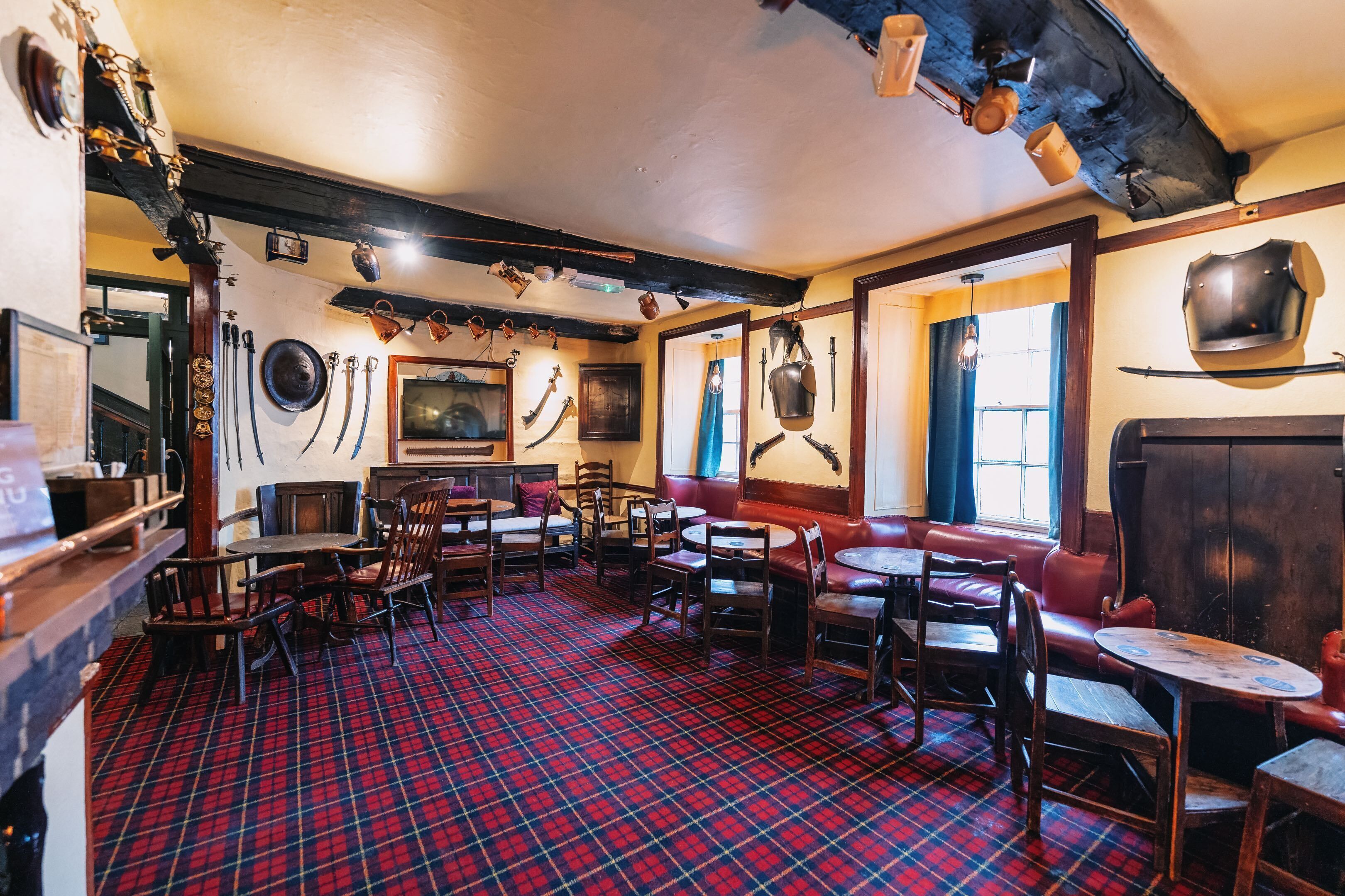 A pub with a red plaid floor, wooden furniture, and various decorations including a shield and a sword on the wall.