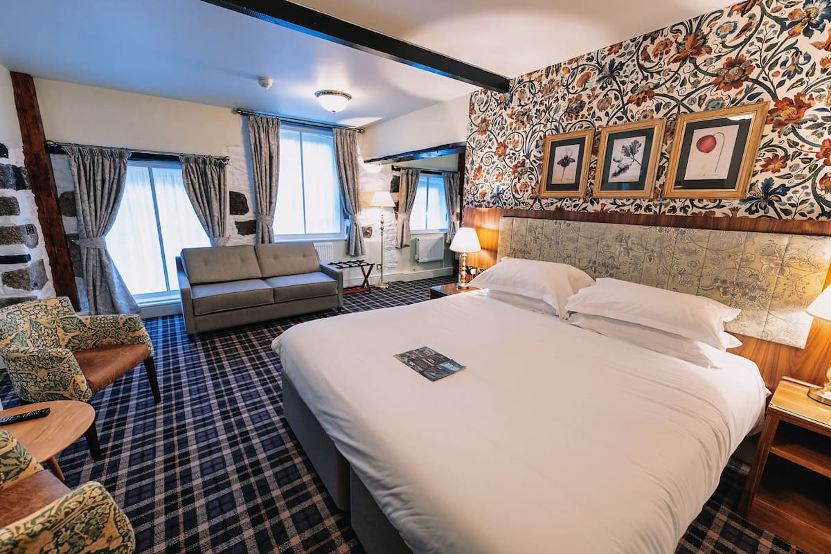 A hotel room with a large bed, a sofa, a chair, a table, and a view of the outside.