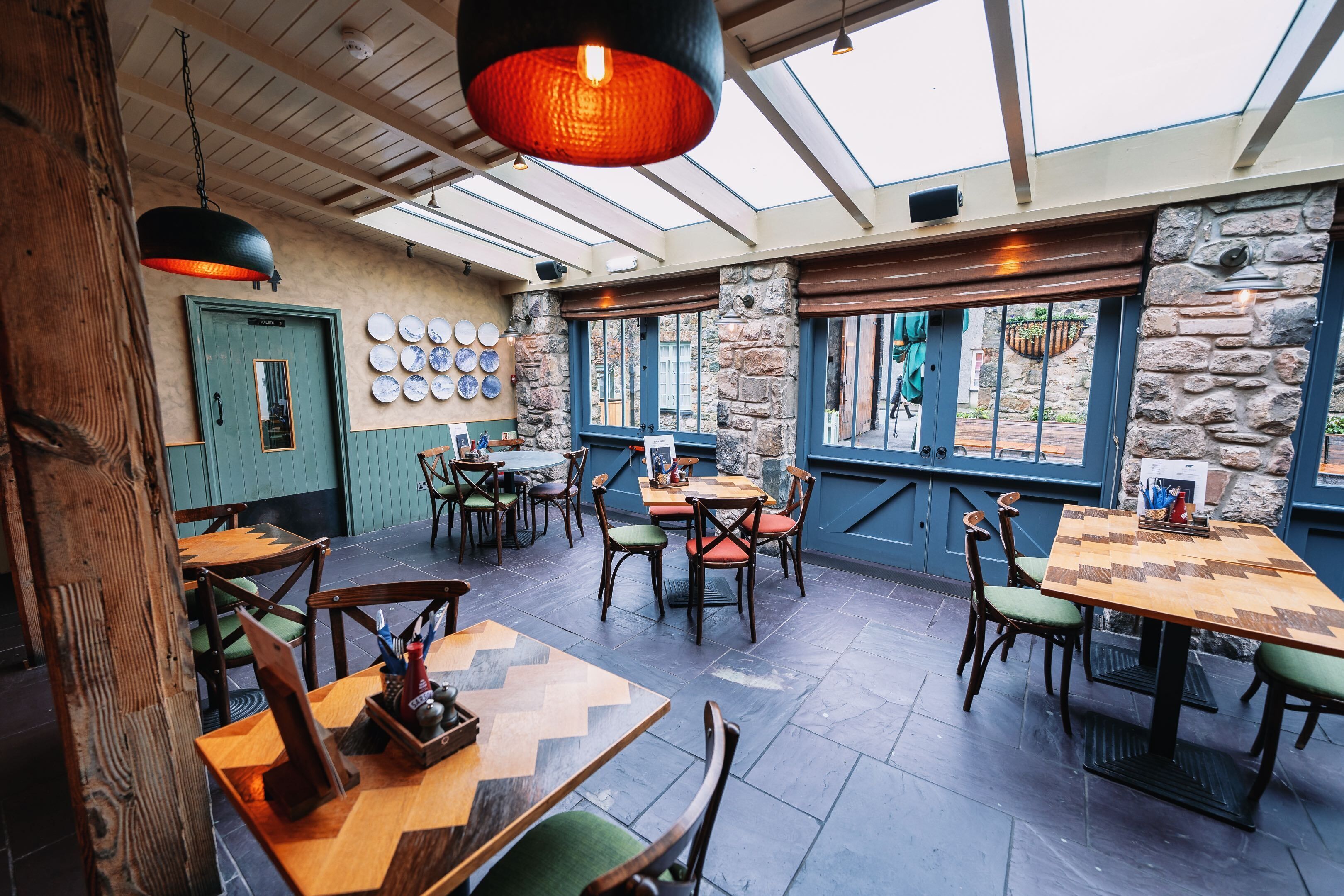 A restaurant with wooden tables and chairs, a green door, and a wall with plates.