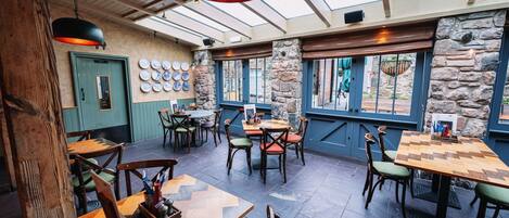 A restaurant with wooden tables and chairs, a green door, and a wall with plates.