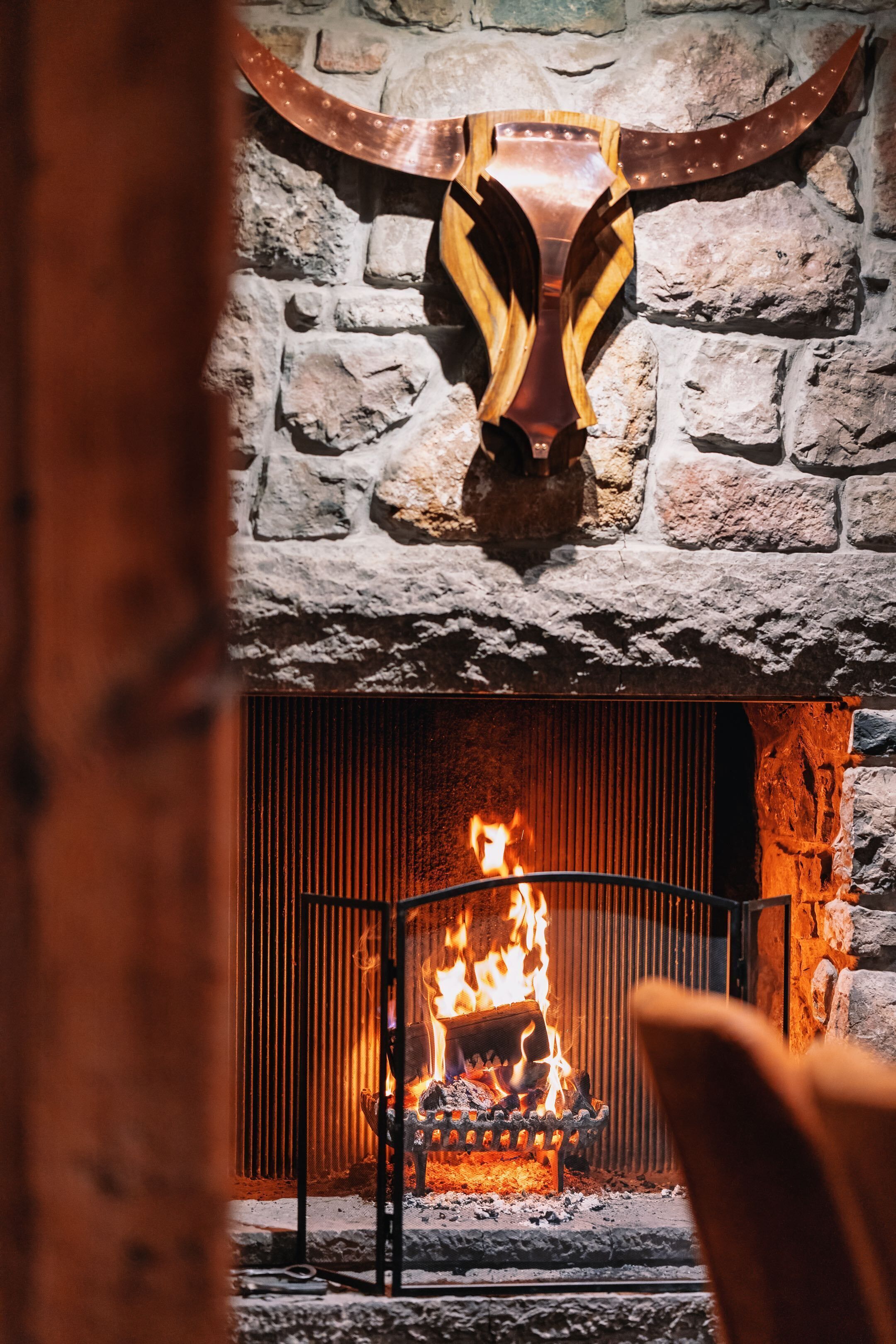 A stone fireplace with a metal fire grate and a large, decorative wooden sculpture above it.