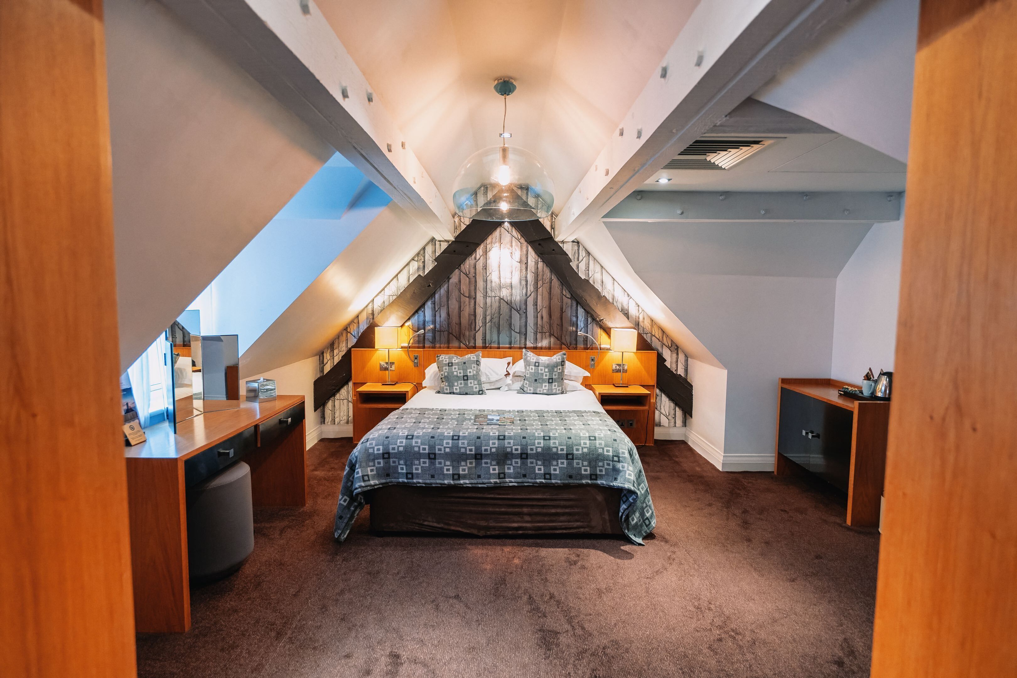 A bedroom with a sloped ceiling, a large bed, two bedside tables, and a desk.