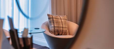 A modern room with a glass table, a white chair with a polka dot cushion, and a large mirror.