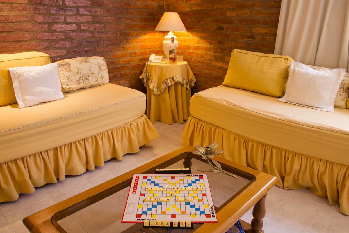 A room with two yellow sofas, a small round table with a board game, and a lamp on a side table.
