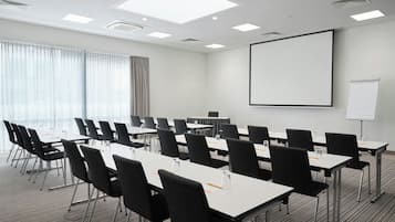 Una sala conferenze con un grande schermo, diversi tavoli e sedie.
