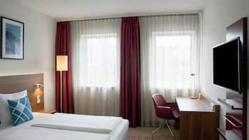 A hotel room with two beds, a desk, a chair, a TV, and curtains.