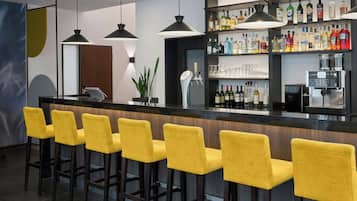 A bar area with a long counter, multiple yellow bar stools, and a variety of liquor bottles on shelves.