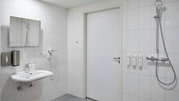 Un baño moderno con un lavabo blanco, un espejo, una ducha y artículos de aseo en la pared.