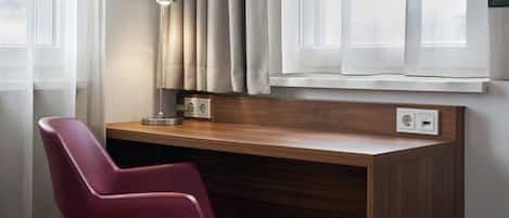 Una habitación moderna con un escritorio de madera, una silla roja y un ventanal con cortinas traslúcidas.
