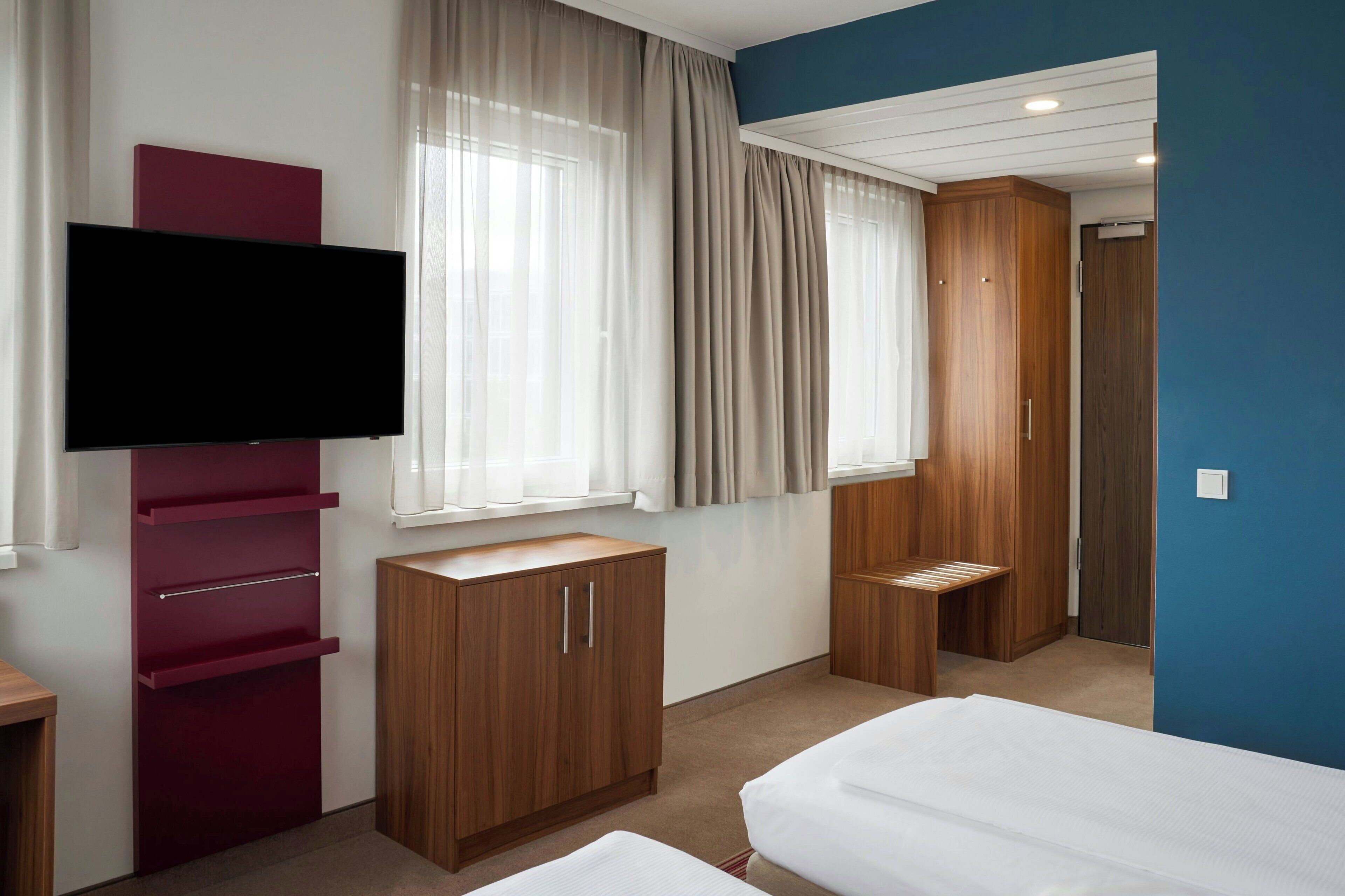 Ein Hotelzimmer mit Bett, Fernseher, Kleiderschrank und Schreibtisch.