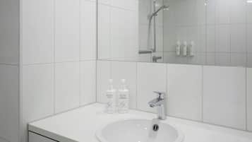 A modern bathroom with white tiles, a sink, a mirror, and two bottles of Activ brand shampoo.