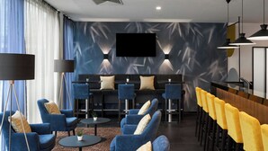 A modern lounge area with blue armchairs, a bar with yellow stools, and a flat-screen TV mounted on the wall. - Four Points Flex by Sheraton Essen (Essen)