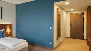 A hotel room with a bed, a wooden wardrobe, a mirror, and a door leading to another room.
