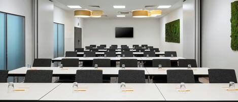 Un salón de conferencias con mesas blancas, sillas negras y una pantalla grande en la pared.