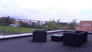 Une terrasse sur le toit avec un plancher en bois foncé, deux canapés en rotin noir et une table basse en verre.