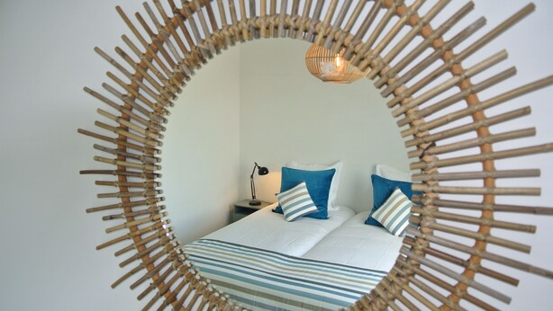 Un lit avec une literie à rayures, un miroir rond encadré de bambou et une lampe de chevet.