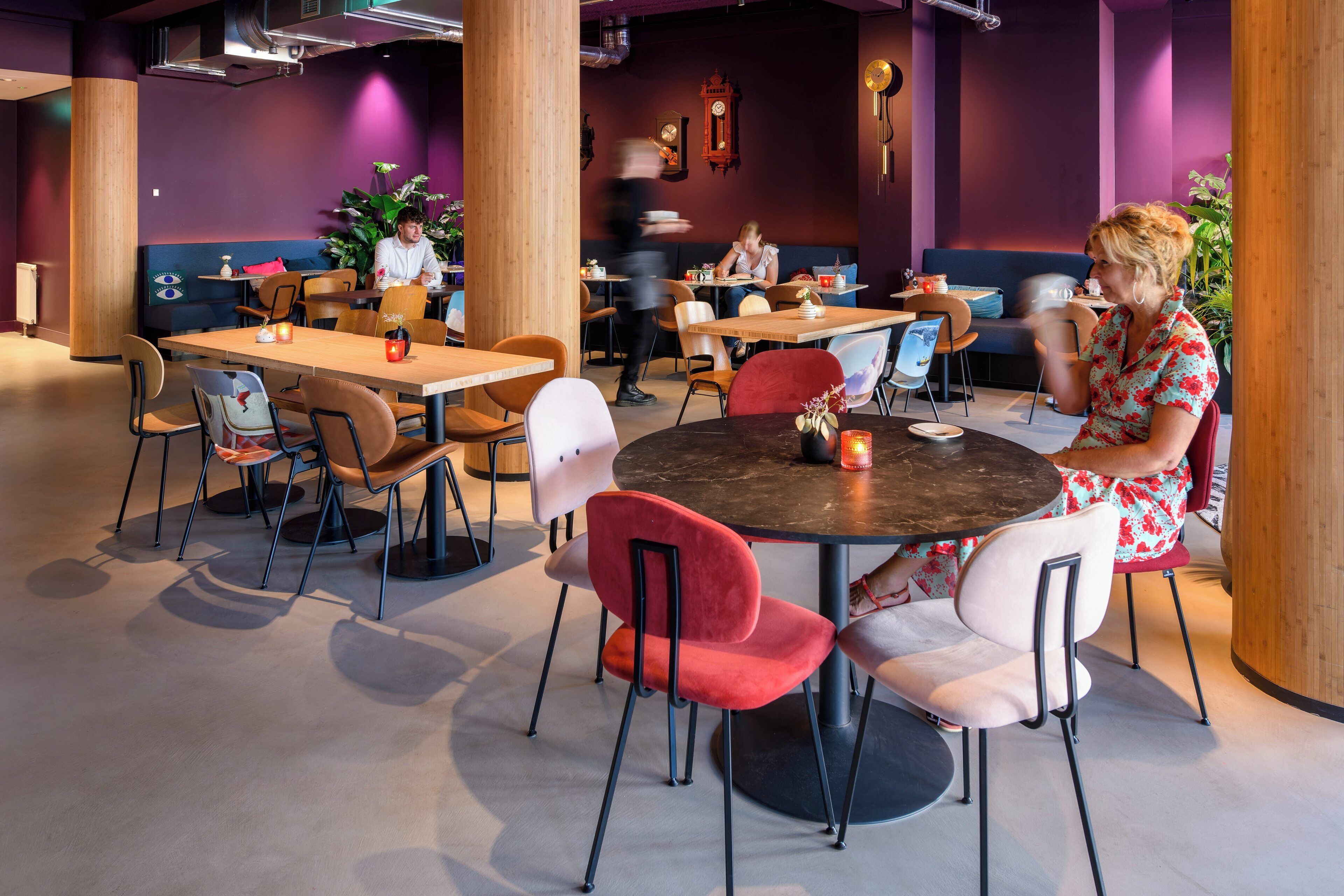 A modern dining area with round tables and chairs, wooden pillars, and purple walls.