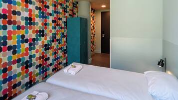 Habitación de hotel con dos camas, un pared con un estampado de lunares y un armario color turquesa, y una puerta al fondo.