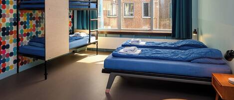 A room with bunk beds, a round table, and a view of a brick building through a window.