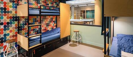 Une chambre avec des lits superposés, un bureau et un mur décoré de motifs à pois colorés.