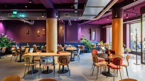 A spacious indoor dining area with multiple tables and chairs, large wooden pillars, and potted plants. - Stayokay Utrecht Centrum - Hostel (Utrecht)