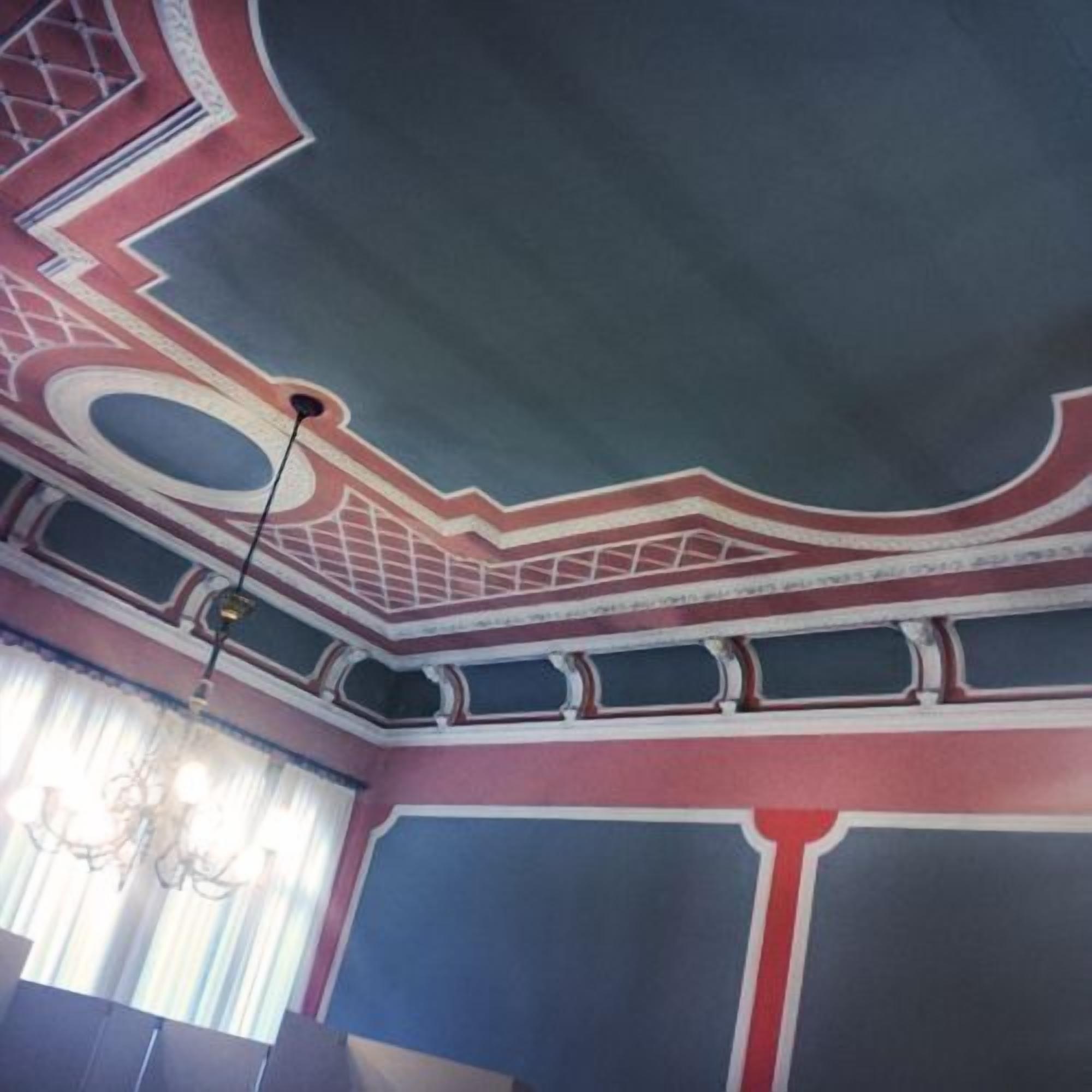 Ein Zimmer mit dekorativer Decke, die geometrische Muster und eine Chandelüster zeigt.