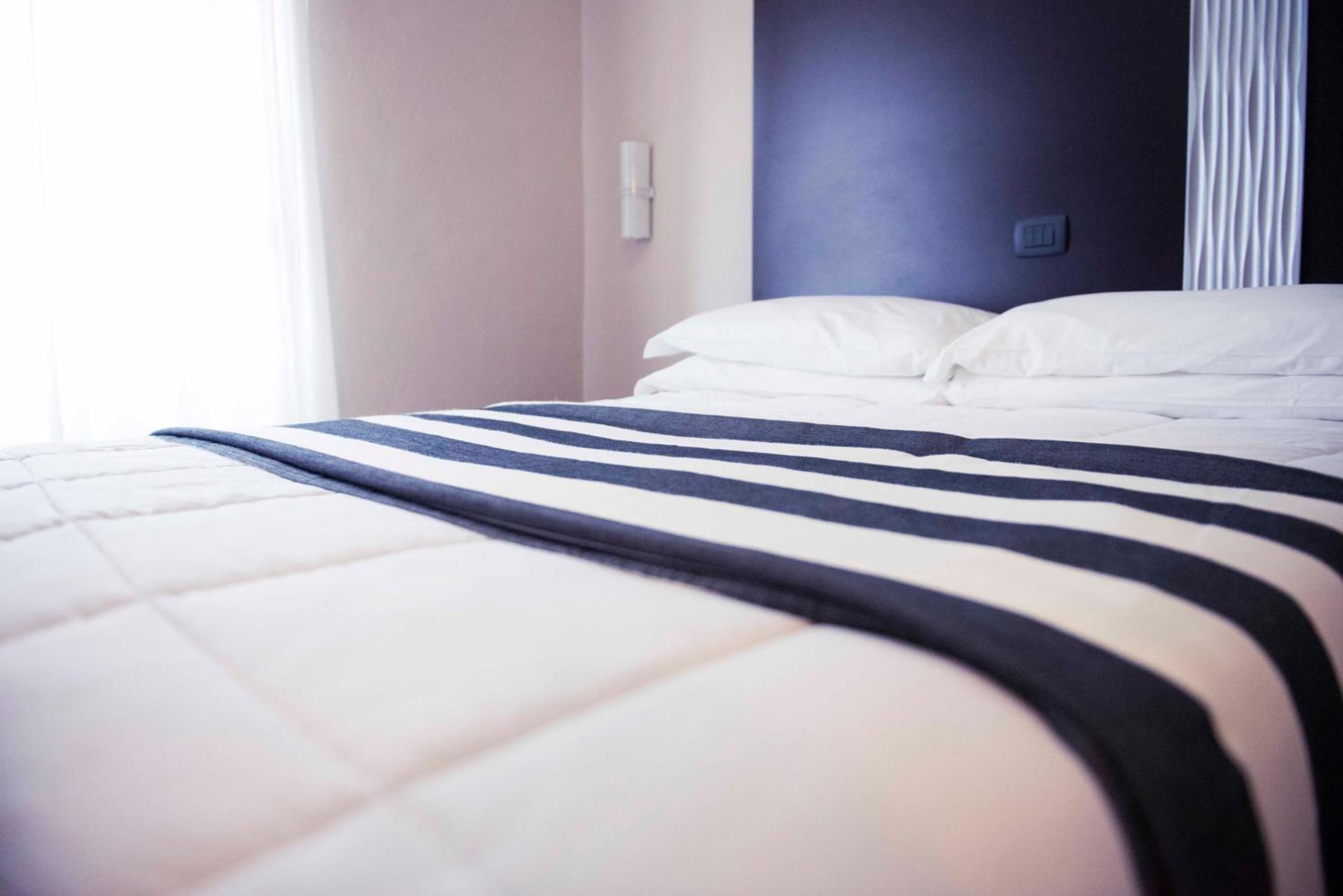 Ein ordentlich bezogenes Bett mit einer gestreiften Tagesdecke und weißen Kissen in einem Hotelzimmer.