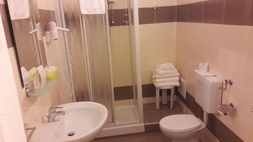 Ein Badezimmer mit einer Duschkabine, einem Waschbecken, einer Toilette und einem Stapel weißer Handtücher.