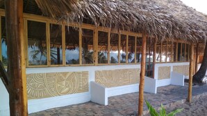 A beachside building with a thatched roof, white walls with decorative panels, and a brick-paved area. - Duna Lodge (Jangamo)