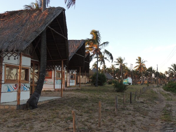 A beachfront property with thatched-roof structures, a sandy path, and palm trees.