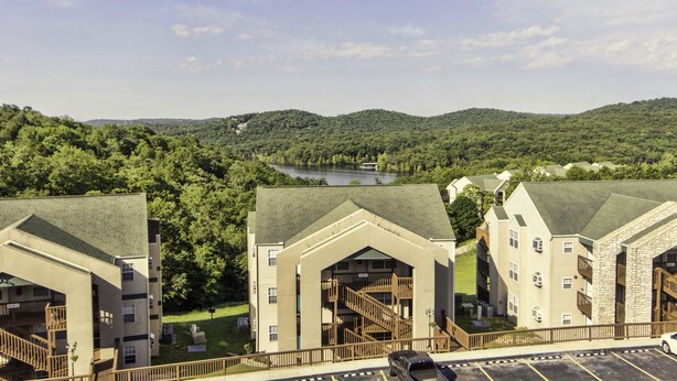 A hotel with multiple buildings, a parking area, and a view of a lake surrounded by hills. - Branson Condo Resorts Silver Dollar City (Branson)
