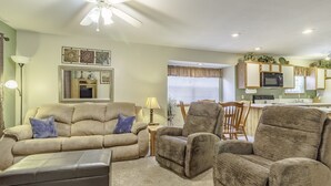 A living room with a beige sofa, a brown armchair, and a coffee table. There is a ceiling fan, a lamp, and a window with blinds. - Branson Condo Resorts Silver Dollar City (Branson)