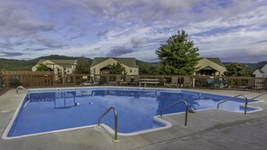 A swimming pool with lounge chairs and tables, surrounded by wooden fences and buildings with green roofs. - Branson Condo Resorts Silver Dollar City (Branson)