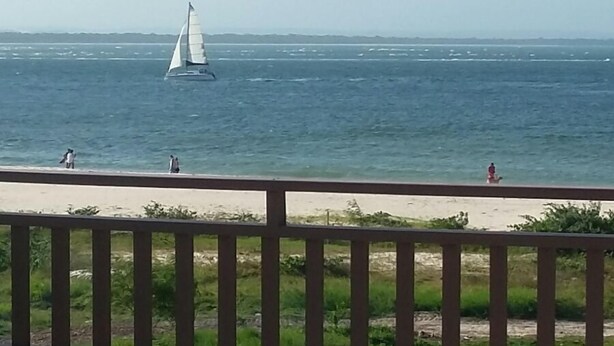 Uitzicht op zee vanaf een balkon, met een tafel, stoelen en een hekwerk, plus een zeilboot op het water.