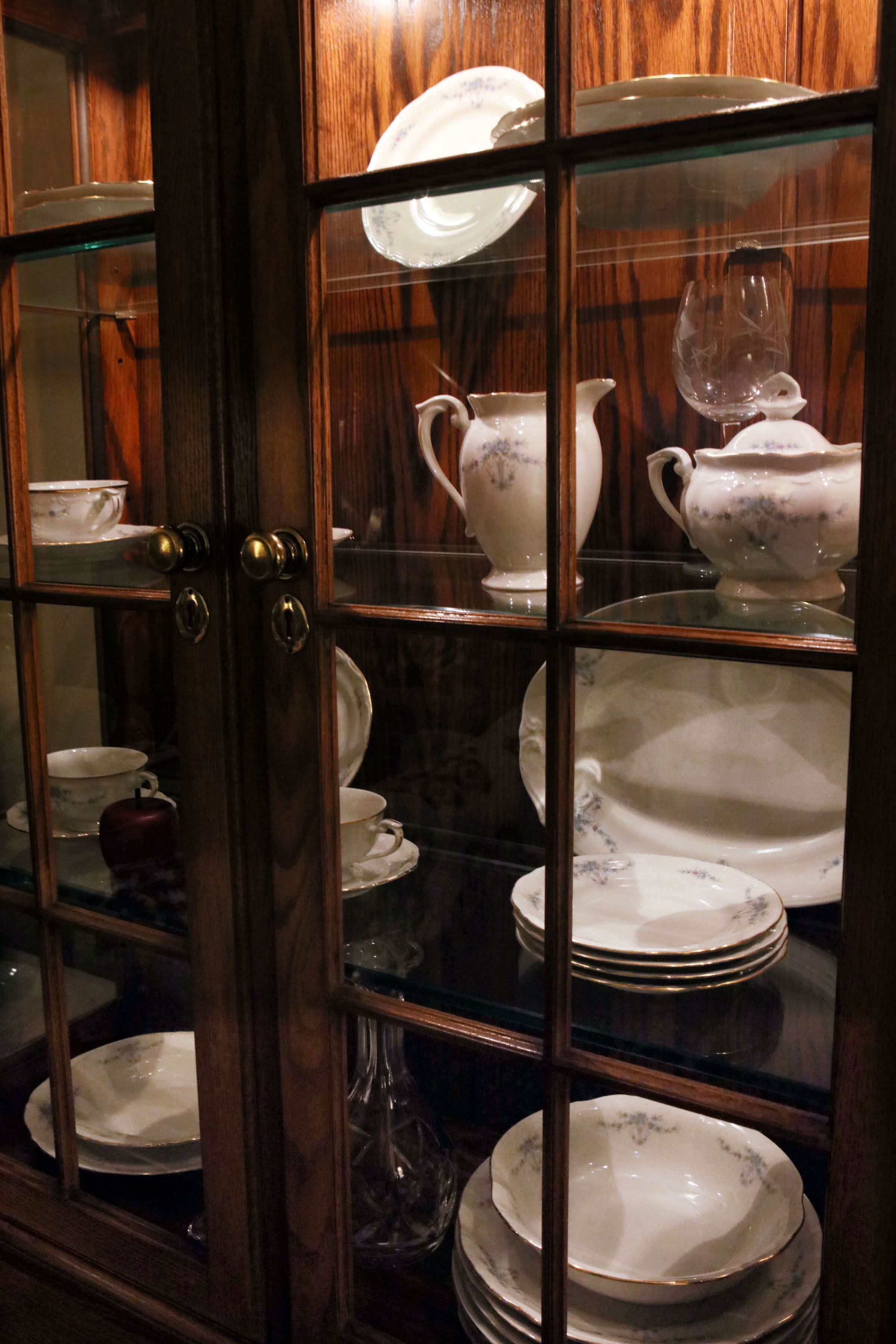 A glass-fronted cabinet with various white ceramic dishes and a single red teapot.