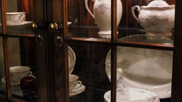 A glass-fronted cabinet with various white ceramic dishes and a single red teapot.