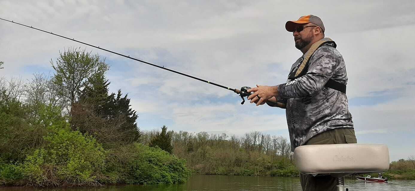A person fishing by a river with a boat docked nearby.