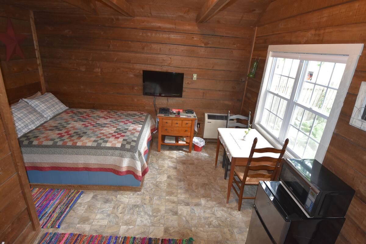 A cozy cabin room with a bed, a desk, a television, and a window.