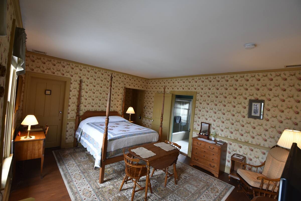 A bedroom with a four-poster bed, a wooden desk, a chair, a dresser, and a mirror.