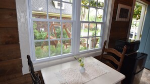 Una cocina con una mesa blanca, un jarrón con flores y vistas a un jardín a través de amplios ventanales.