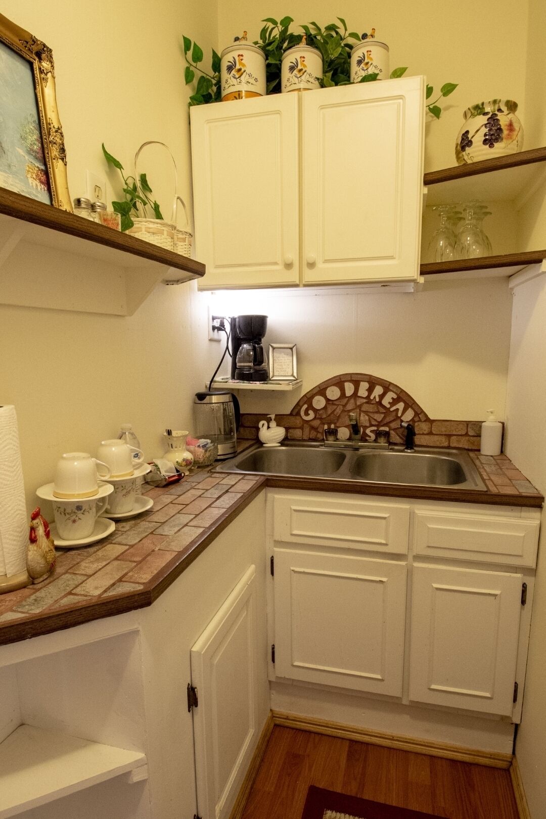 A kitchen with white cabinets, a coffee maker, and a decorative sign above the sink.