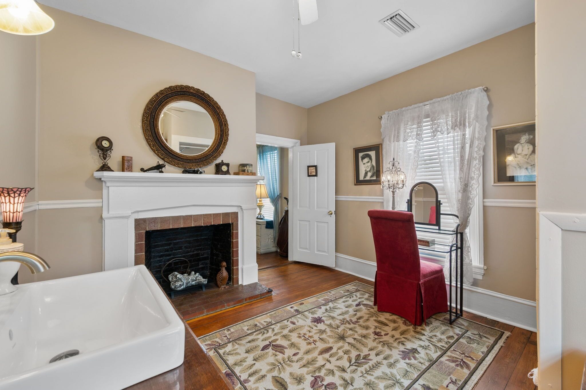 A room with a fireplace, a mirror, a red chair, and a large window with curtains.