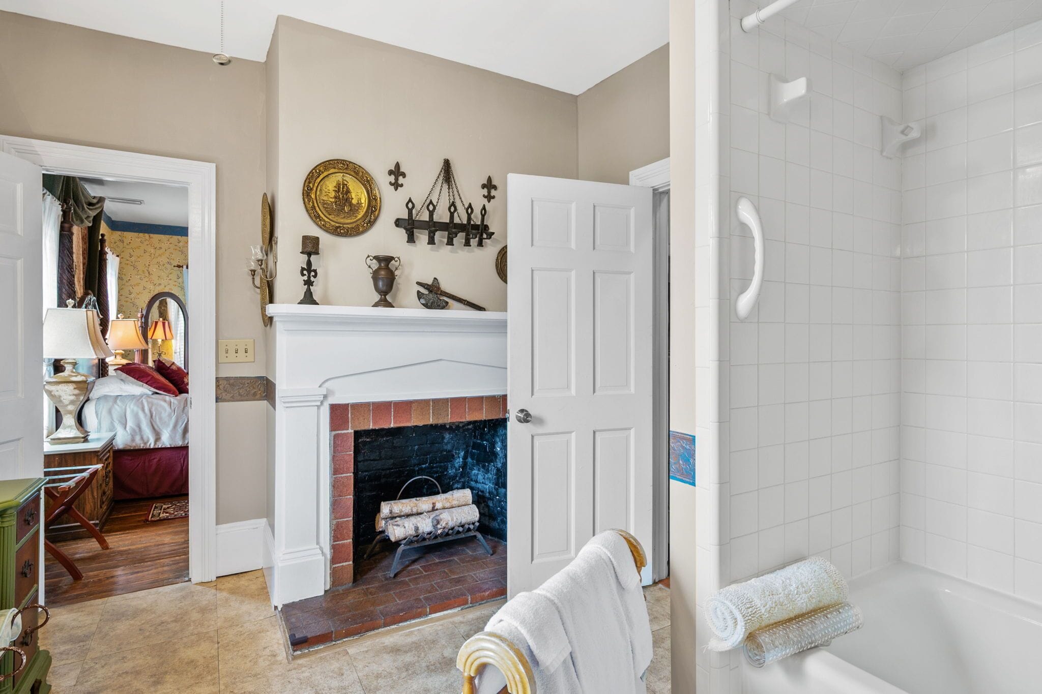 A room with a fireplace, a bed, a bathroom with a bathtub, and a hallway leading to another room.