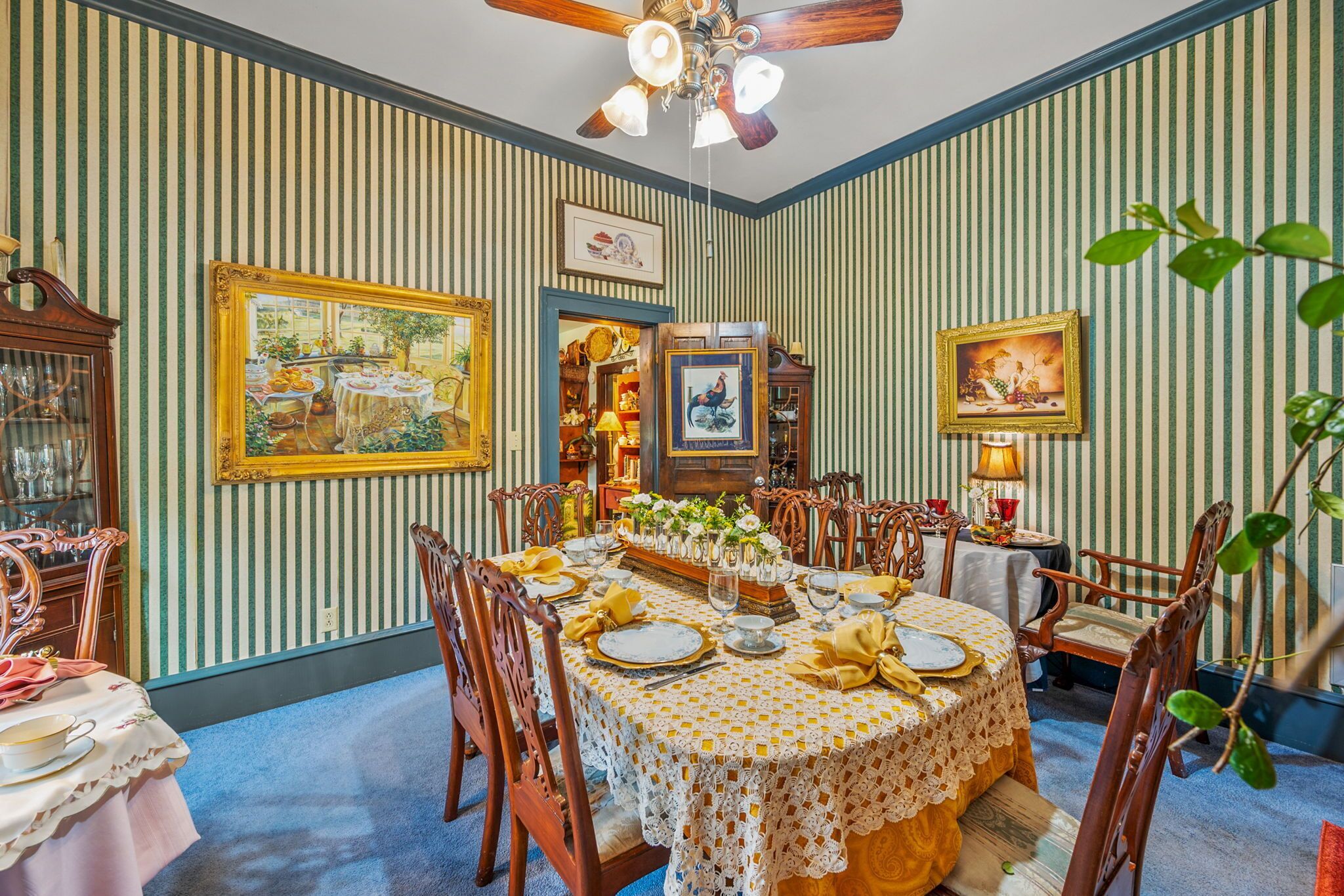 A dining room with striped wallpaper, wooden furniture, and a ceiling fan.