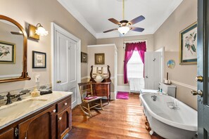 A bathroom with a wooden floor, a clawfoot bathtub, a vanity with a mirror, and a ceiling fan.