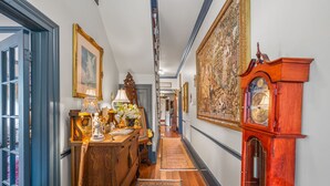 Un pasillo con pisos de madera, un reloj grande y obras de arte enmarcadas en las paredes.