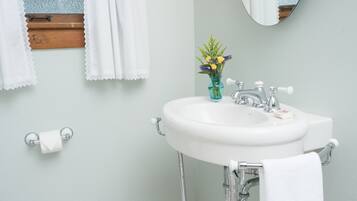 A bathroom with a white sink, a mirror, a window with lace curtains, and a vase with flowers.